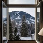 Open window view of snowy mountain landscape and pine trees